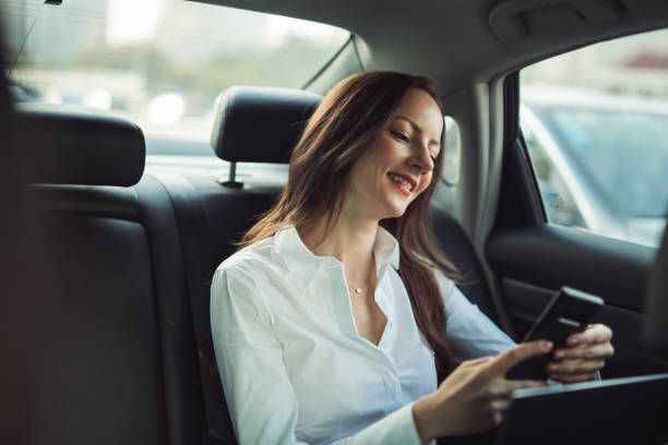 businesswoman using laptop and mobile phone in backseat of a car.